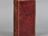 an old book with a red cover sitting on top of a table