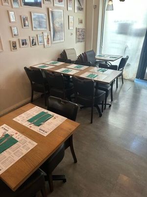 Des tables et des chaises sont alignées dans une pièce où sont accrochés des tableaux aux murs.