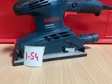 une ponceuse orbitale Bosch posée sur une table, à côté d'une boîte rouge