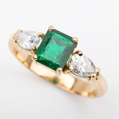 an emerald and diamond three stone ring on a white background