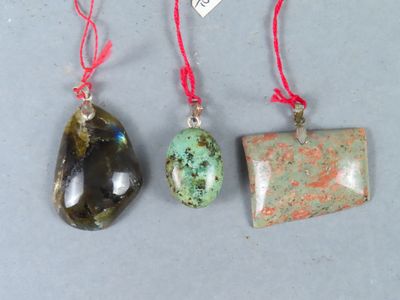 trois types différents de pendentifs avec un cordon rouge sur un fond gris