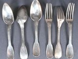 cinq cuillères en argent et deux fourchettes sont alignées sur une table