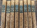 six old books are lined up in a row on a table