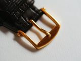 black leather belt with gold buckle laying on a white surface
