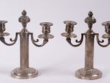 une paire de bougeoirs plaqués argent sur des socles, sur fond blanc
