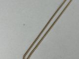 un collier en or muni d'une chaîne, posé sur une surface blanche