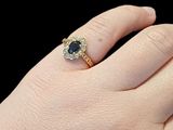 woman ' s hand wearing a gold ring with a blue sapphire and diamonds