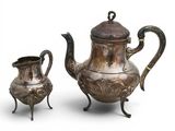two silver teapots and a cup on a stand on a white background