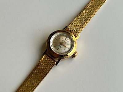 une image représentant une montre en or avec un cadran blanc posée sur une surface blanche