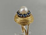 a close up of a gold ring with a pearl and blue sapphires