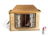 a small doll sitting in a doll house made out of wood