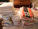 une pile de serviettes pliées sur un lit, dans une chambre où se trouve une commode
