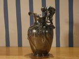 a silver vase sitting on a wooden table with a striped wall behind it