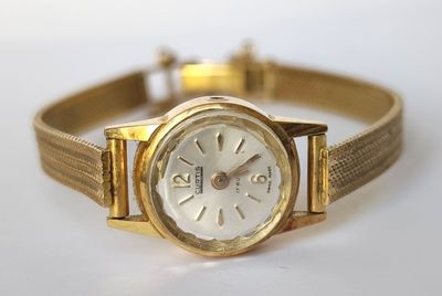gros plan d'une montre en or sur une surface blanche