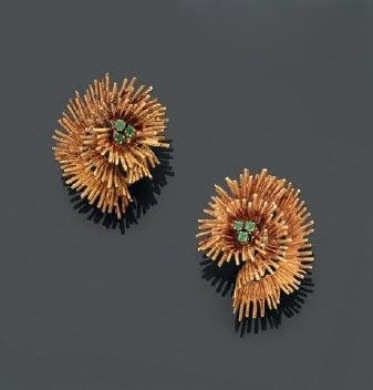 une paire de boucles d'oreilles en or et émeraude posées sur un fond noir