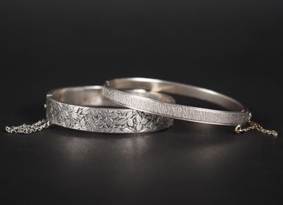 une paire de bracelets en argent posés sur une surface noire