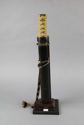 a close up of a black and gold samurai sword on a wooden stand