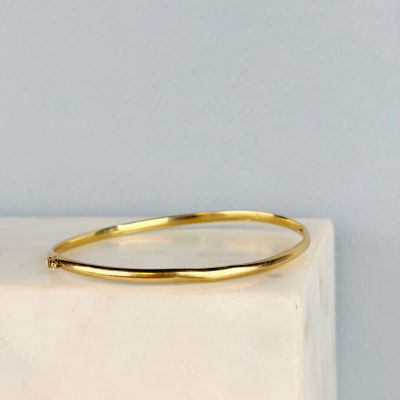 un gros plan d'un bracelet rigide en or posé sur un bloc de marbre