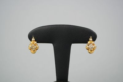 une paire de boucles d'oreilles en or et diamants posée sur un socle noir