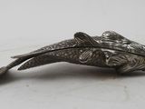 a silver fish brooch on a white surface