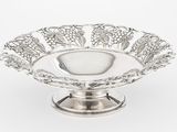un plat ancien en argent, orné de raisins et de feuilles, posé sur un socle