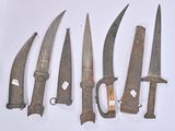 five old knives are lined up on a white surface