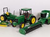 three toy tractors and a raker on a white surface