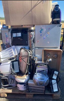 un tas d'appareils électroniques posé sur une palette à côté d'un réfrigérateur