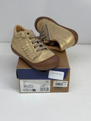 des baskets en cuir doré à lacets posées sur une boîte en carton