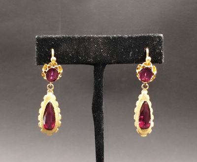 une paire de boucles d'oreilles en rubis et or, posée sur un socle noir