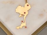 gold plated pendant with a map and ruby stones on a marble surface