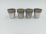 quatre verres à shot en argent posés sur une table blanche