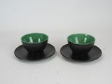 pair of black and green cups and saucers on a white surface