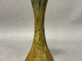 a green and gold vase sitting on a white surface