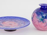 un vase bleu et rose et une assiette posés sur une surface blanche