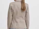 a woman wearing a beige blazer and jeans standing in front of a white background
