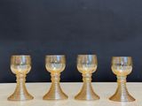 four gold glass goblets sitting on a table with a black background