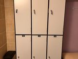 several white lockers in a small room with a bed and a trash can