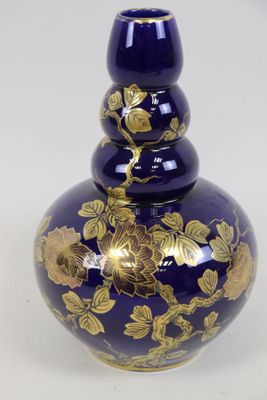 un vase bleu orné de fleurs dorées, posé sur un fond blanc