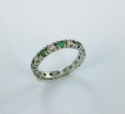 un gros plan d'une bague ornée de pierres vertes sur un fond blanc
