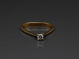 a gold ring with a white diamond on a black surface