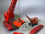 une petite grue rouge en plastique posée à côté d'un morceau de bois rouge