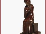 statue d'une femme assise sur un bloc, la main posée sur la poitrine