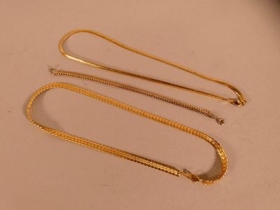 trois colliers en or posés sur une table avec un fond blanc