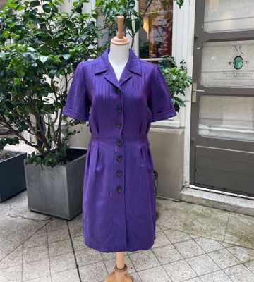 une robe violette posée sur un mannequin devant un immeuble