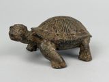 une vieille figurine de tortue en bronze posée sur une surface blanche