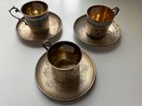 three silver cups and saucers on a white table