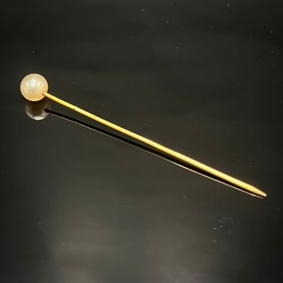 broche plaquée or jaune ornée d'une perle unique sur un fond noir