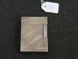 un étui à cigarettes en argent posé sur une surface noire, à côté d'une étiquette