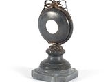 a silver clock that is on a pedestal on a white background